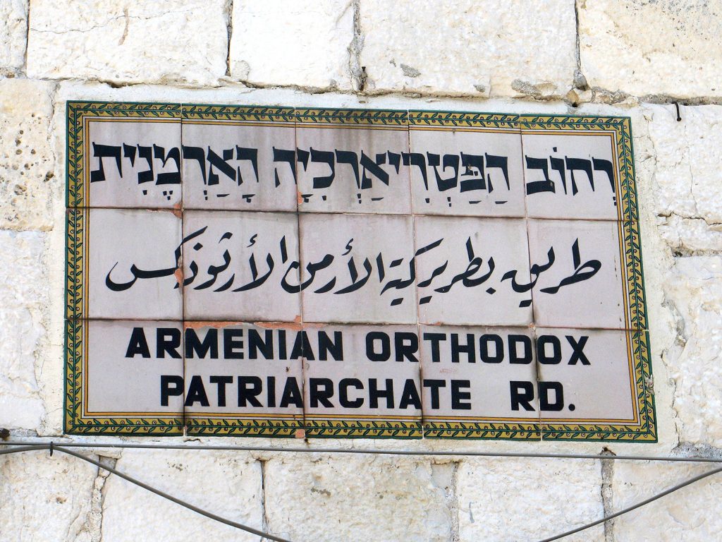 Letrero de mosaico incrustado en una pared de piedra, con escritura en hebreo, árabe e inglés: Armenian Orthodoc Patriarchate Rd.